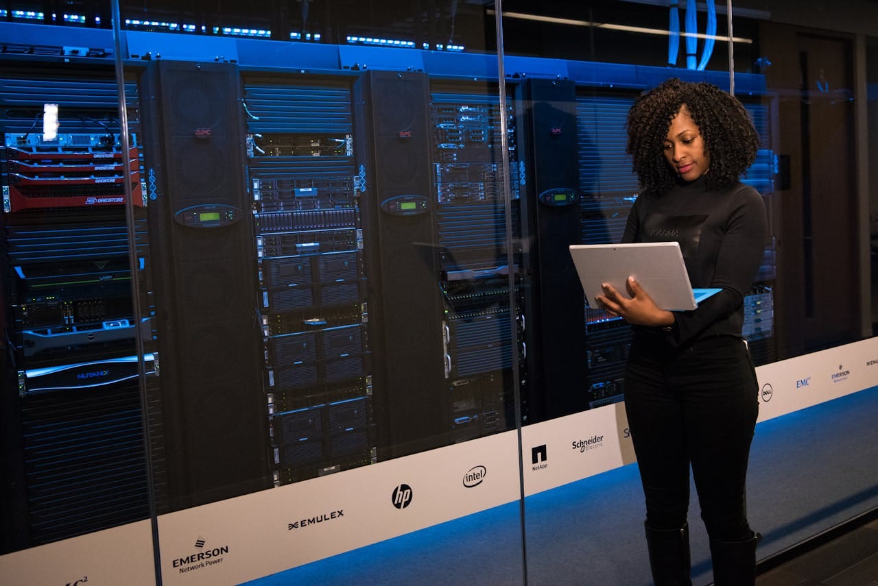Home A female engineer using a laptop while monitoring data servers in a modern server room.